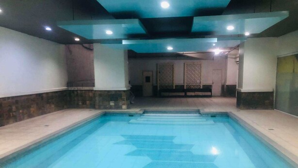A swimming pool with clear blue water, tiled steps leading into it, and a ceiling with recessed lighting. - 2bedroom condo in enjoyable Quezon City with WiFi, AC (Quezon City)