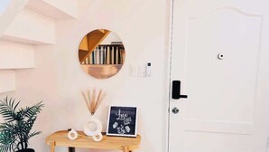 A white door with a black handle, a round mirror on the wall, a small wooden table with a framed picture, and a potted plant. - 2bedroom condo in enjoyable Quezon City with WiFi, AC (Quezon City)
