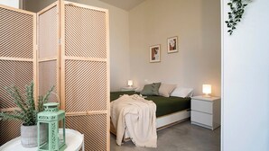 Une chambre à coucher comprenant un lit, des tables de chevet, une commode, un paravent décoratif et une plante en pot.