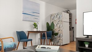 Una sala de estar moderna con un sofá, dos sillones, una mesita, un mueble para TV y una cocina con armarios y un refrigerador.