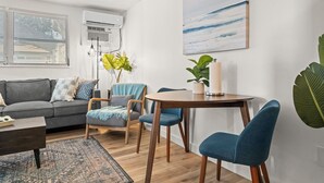 Una sala de estar moderna con un sofá gris, sillas azules, una mesa de centro de madera y una mesa redonda con una planta en maceta.