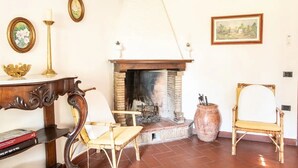 Una habitación con chimenea, dos sillones, una mesa con una vela y cuadros en la pared.