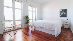A bedroom with a bed, a chair, a potted plant, and a bedside table.