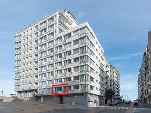 A modern multi-story building with a flat facade, large windows, and a corner entrance. - Apartment With Side sea View (Ostend)