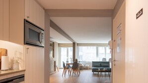 A modern kitchen with a built-in microwave, a dining area with a table and chairs, and a living room with a sofa and a coffee table. - Apartment With Side sea View (Ostend)