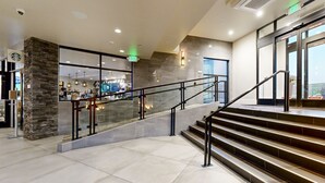 A modern hotel lobby with a Starbucks, a staircase, and a glass elevator.