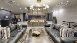 A modern lobby with leather sofas, a central fire feature, and a chandelier.