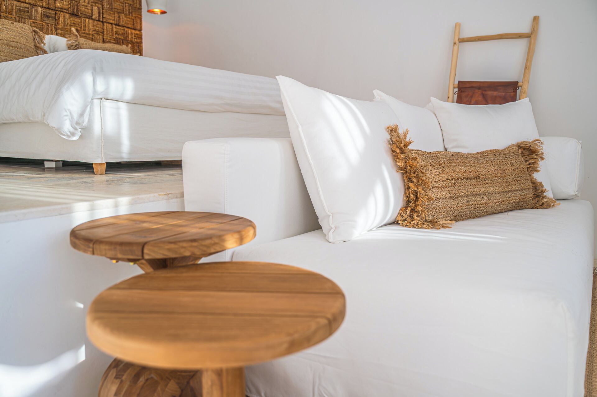 Une chambre d’hôtel moderne avec un canapé blanc, un tabouret en bois et un lit recouvert de draps blancs.