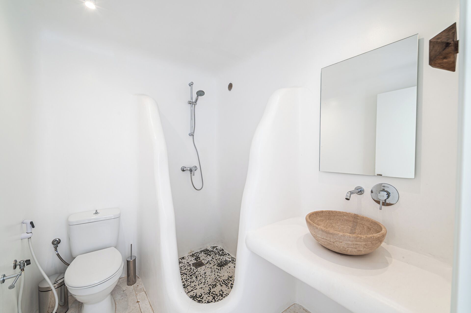 A modern bathroom with a white toilet, a shower, and a sink with a wooden bowl.