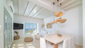 A bright, airy room with a large window, a wooden ceiling, a dining table with chairs, and a wall-mounted TV. - Anthis Villas Mykonos (Mykonos)
