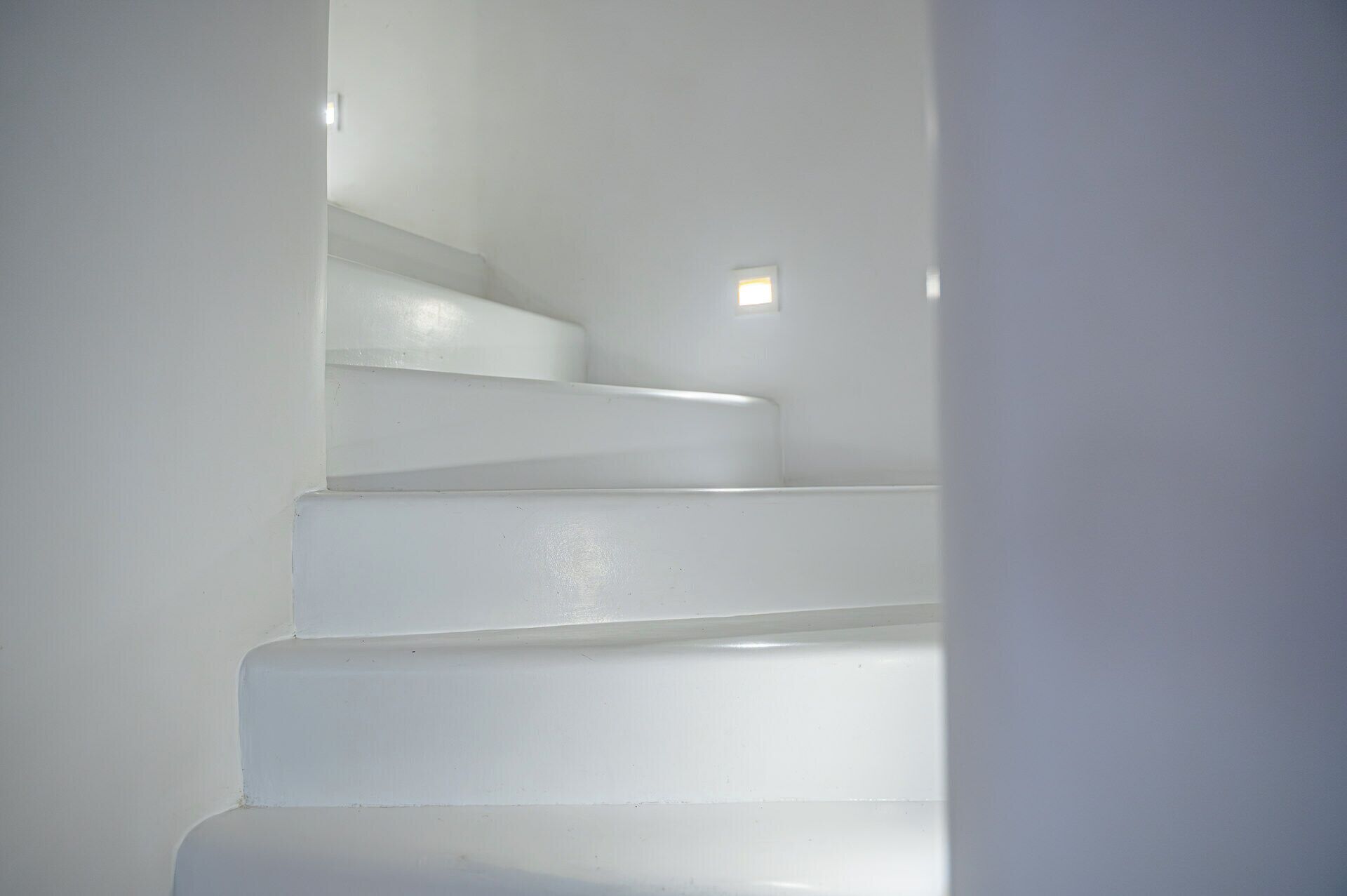 Un escalier avec des murs blancs et une petite fenêtre en haut.