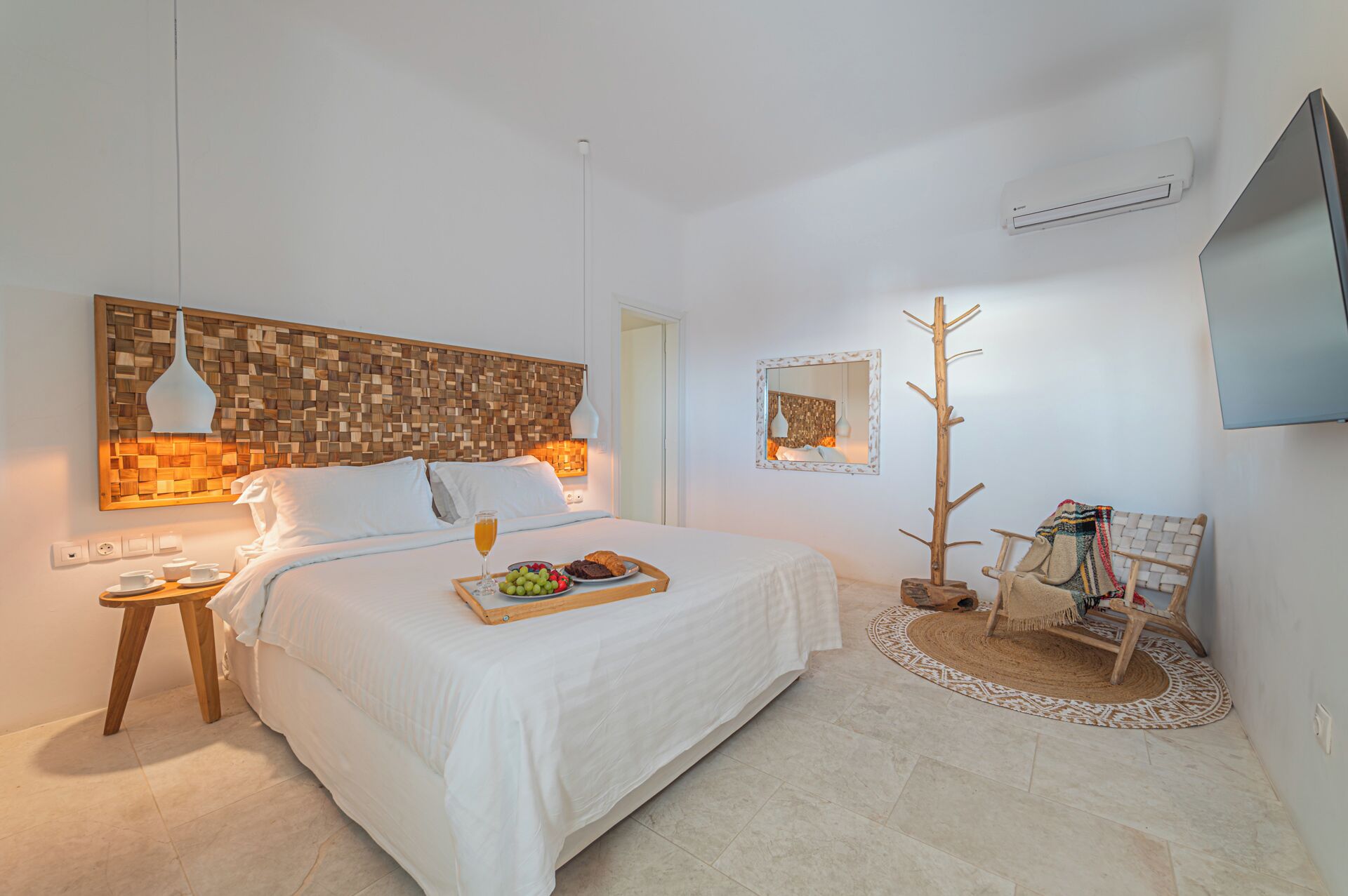 Un dormitorio moderno con una cama grande, mesitas de noche, un espejo, un perchero de madera y un televisor.