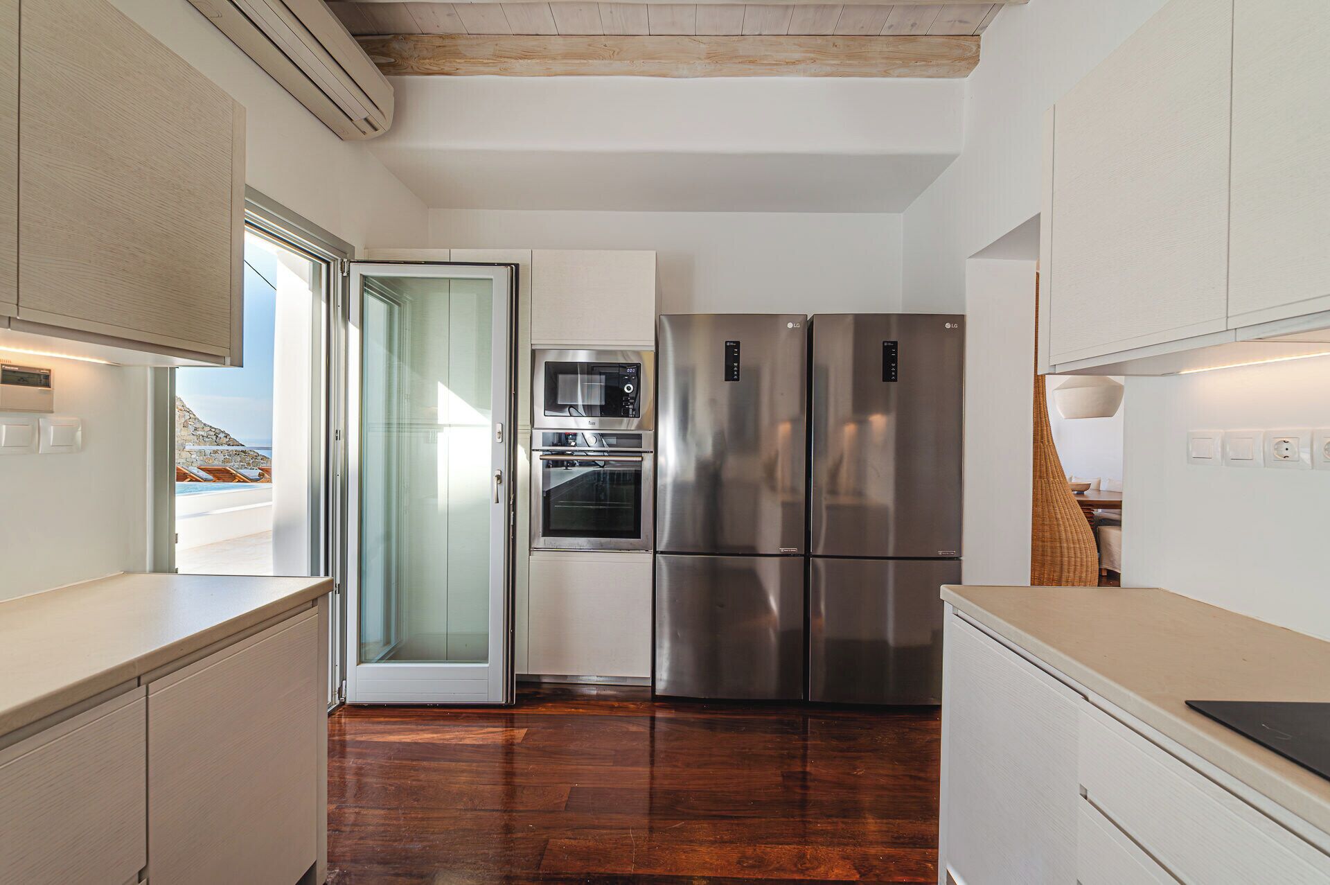 A modern kitchen with stainless steel appliances, a glass door leading to a balcony, and wooden flooring.
