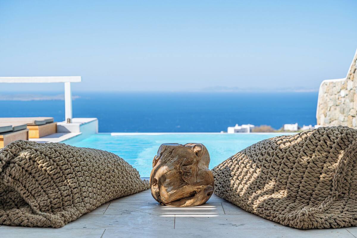 Zona junto a la piscina con vista al mar, que incluye dos espacios amplios con asientos texturizados y una escultura de piedra.