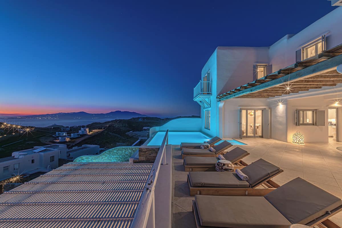 Una villa moderna con piscina en la azotea, tumbonas y vista al mar al atardecer.