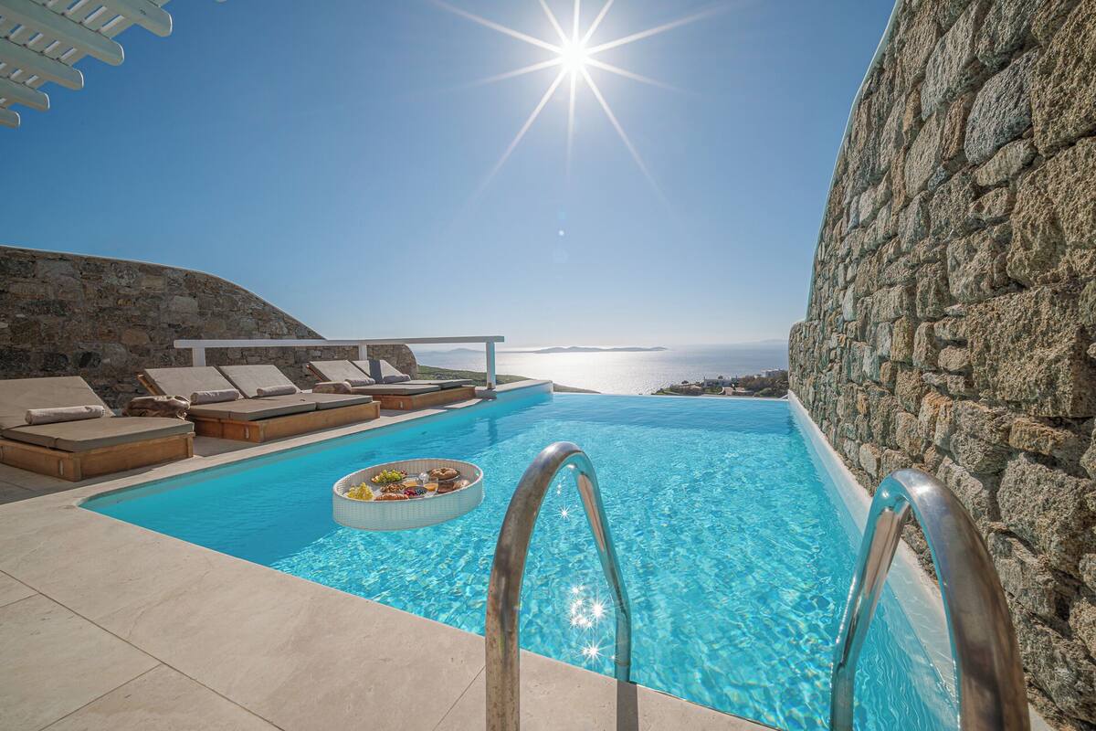 Zona junto a la piscina con sillones de descanso, solárium y vista al mar.
