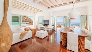 A spacious living area with a wooden floor, white furniture, a large window overlooking the sea, and a modern ceiling design. - Anthis Villas Mykonos (Mykonos)
