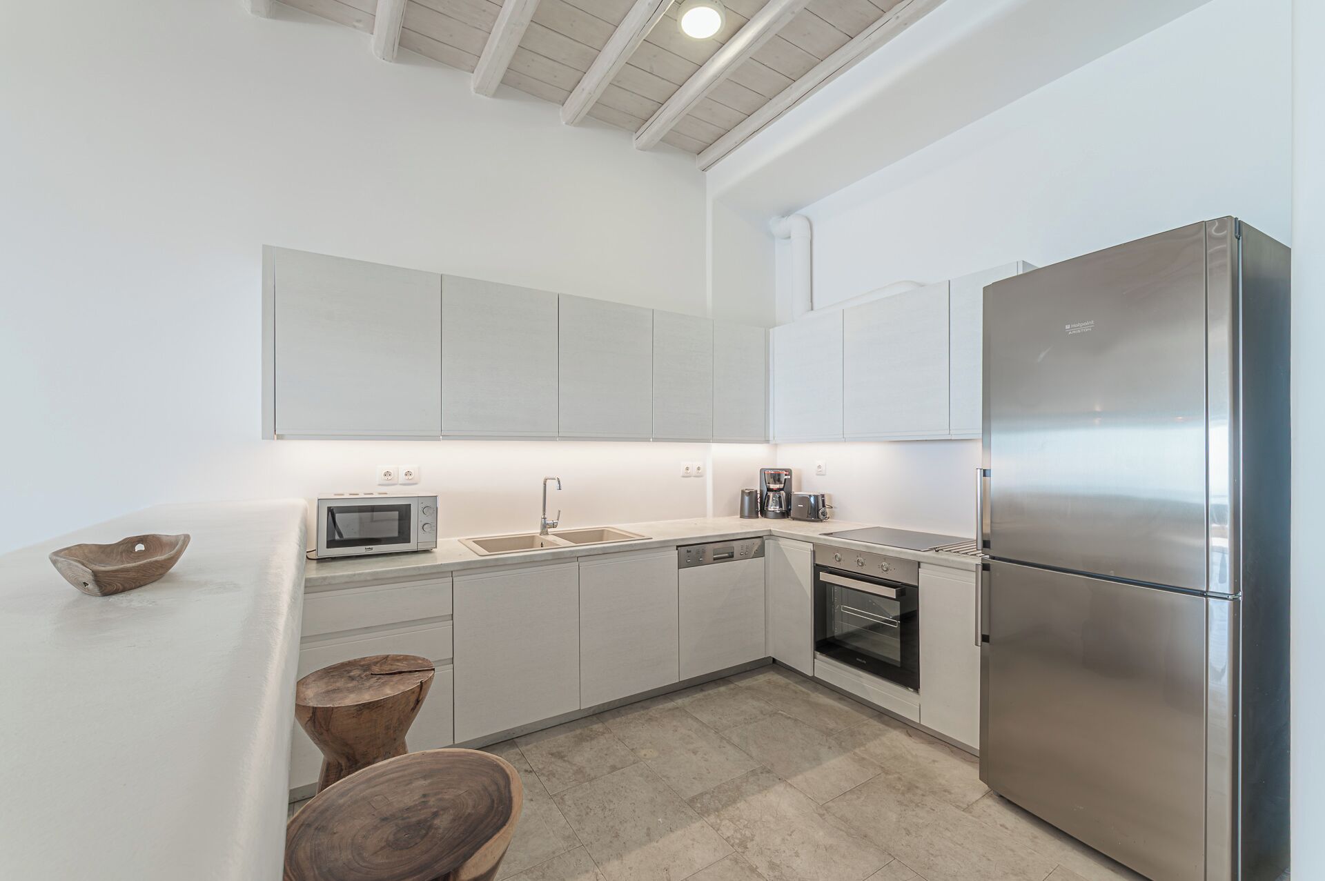 A modern kitchen with white cabinets, a stainless steel refrigerator, a microwave, a coffee maker, and a dishwasher.
