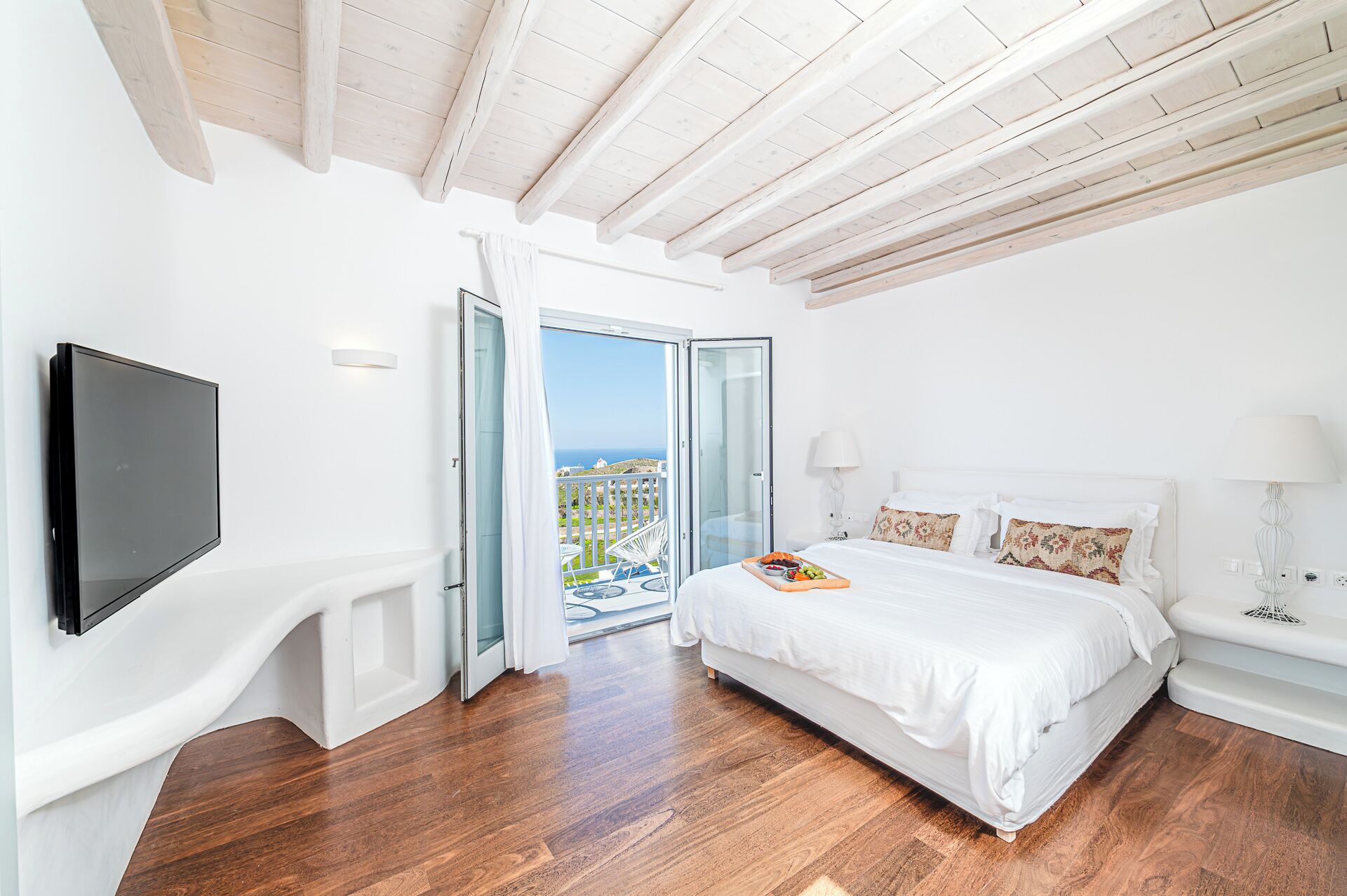 A bedroom with a bed, a TV, and a balcony with a view.