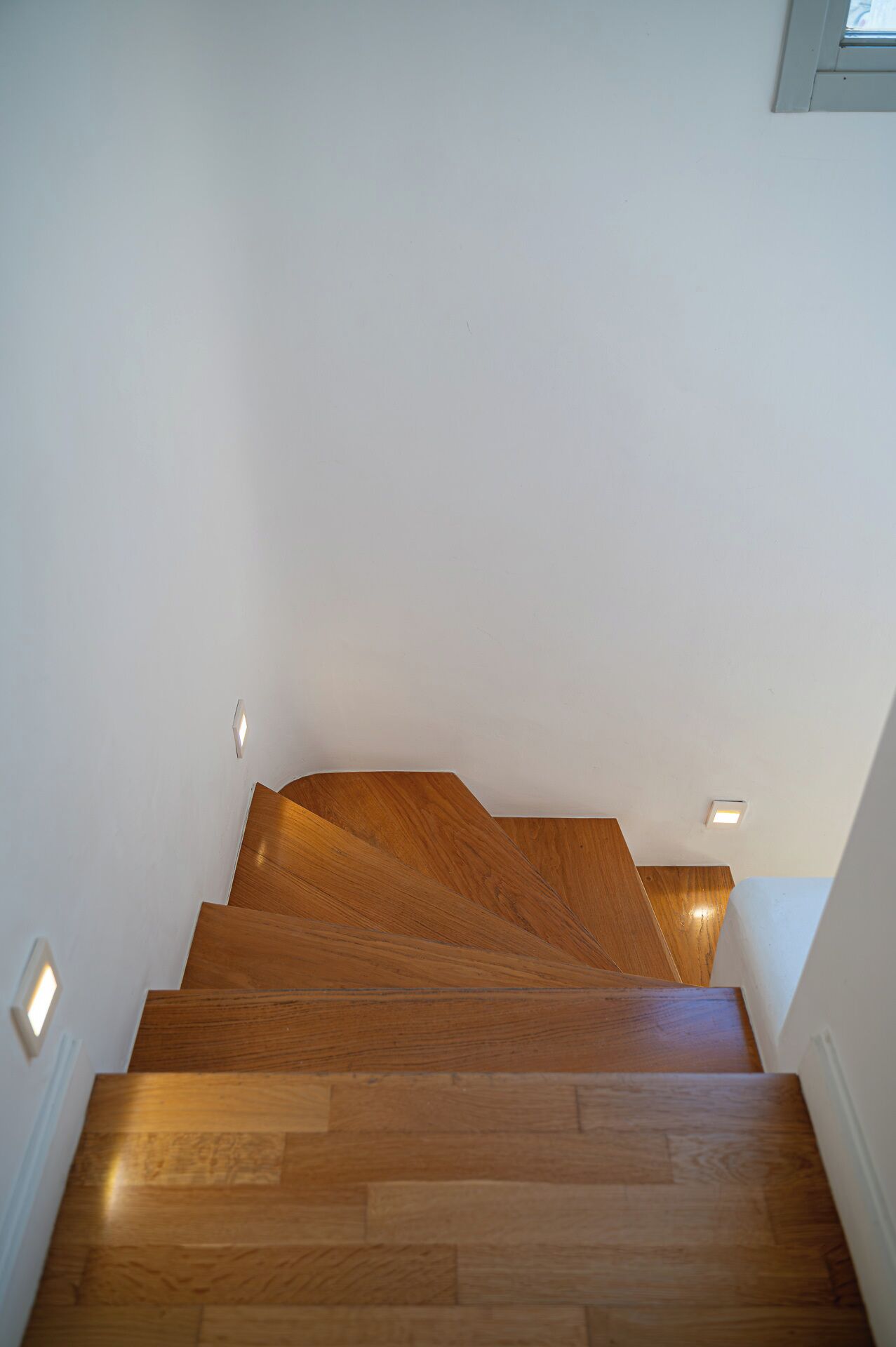 Una escalera de madera con diseño moderno, paredes blancas e iluminación empotrada.