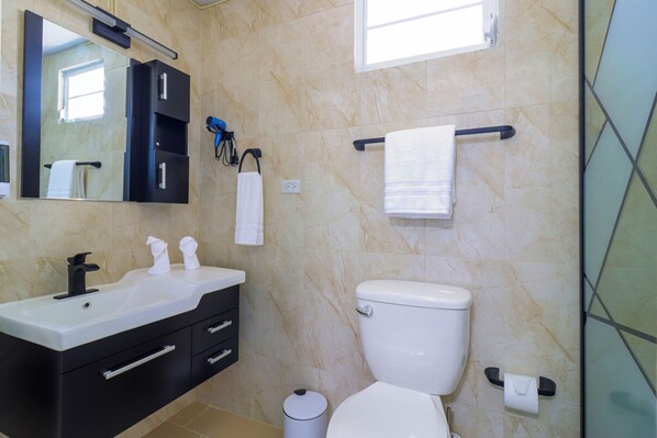 Un baño con lavamanos blanco, tocador negro, inodoro y un perchero para toallas.