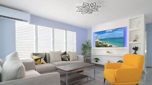 A modern living room with a sofa, armchair, coffee table, and a flat-screen TV mounted on the wall. - Casa Mar Y Sol - Vistamar, PR –  4 Minutes From Airport and 8 minutes to Beaches (Carolina)