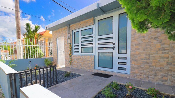 A modern house with a stone facade, a gated entrance, and a small garden with gravel and plants. - Casa Mar Y Sol - Vistamar, PR –  4 Minutes From Airport and 8 minutes to Beaches (Carolina)