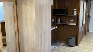 Una cocina compacta con armarios de madera, un microondas, un estante con botellas y un cubo de basura.