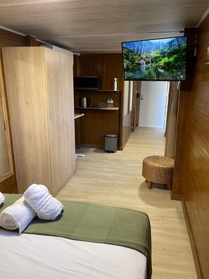 A hotel room with a bed, a television mounted on the wall, a small trash bin, and a wicker stool. - Habitacion Monteazul (El Casar)