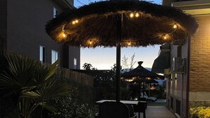 An outdoor patio with a thatched umbrella, chairs, and string lights. - Habitacion Monteazul (El Casar)