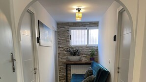 A hallway with a blue sofa, a potted plant, and a wall-mounted light fixture. - Habitacion Monteazul (El Casar)