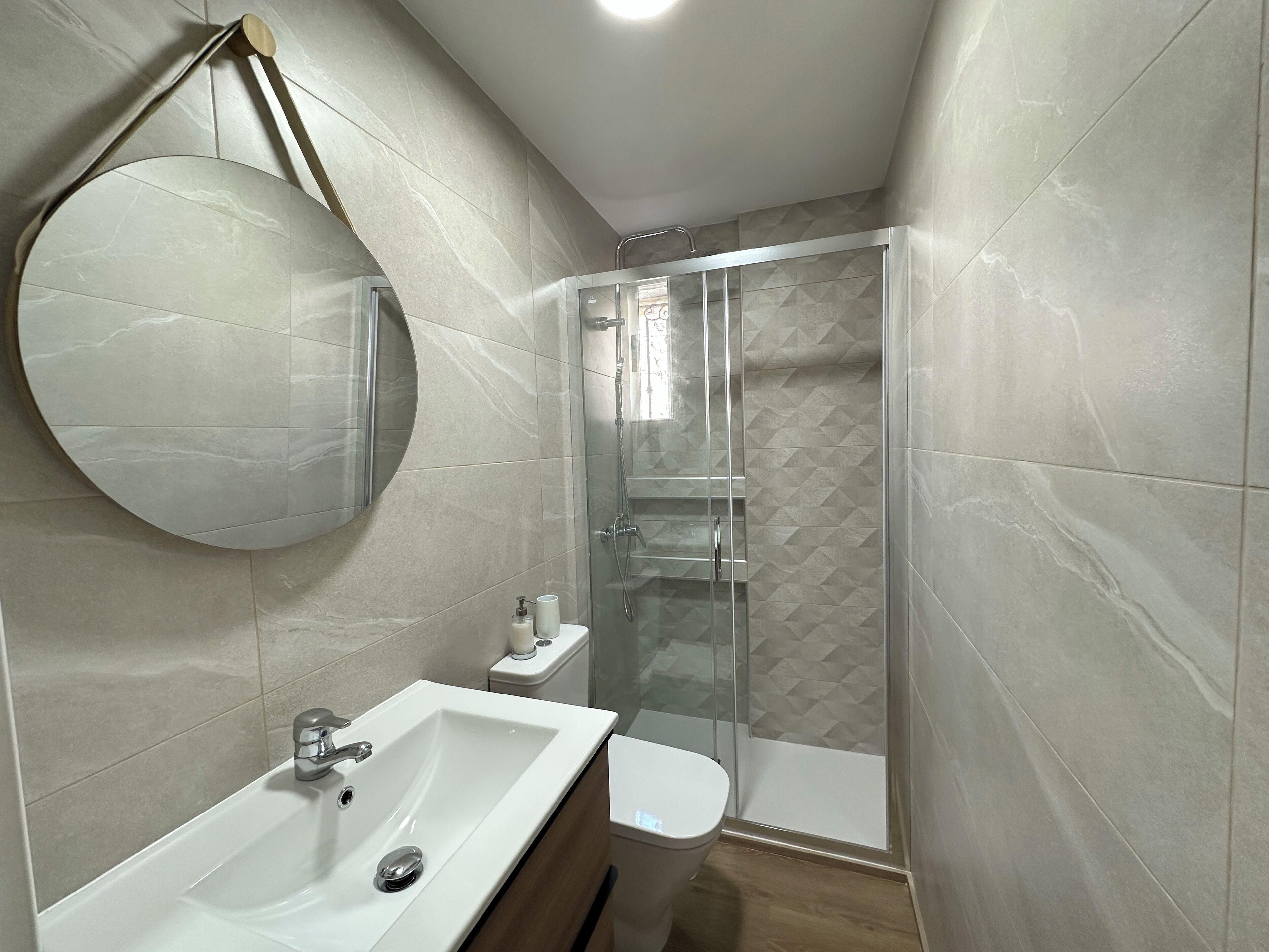 Un baño moderno con un espejo grande, un lavamanos, un inodoro y una ducha con mampara de vidrio.