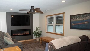 Ein Wohnzimmer mit Kamin, Deckenventilator, großem Fenster und einem gerahmten Bild an der Wand.