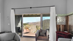 Una habitación con puerta corrediza de vidrio que da a un balcón, una silla estampada de piedritas, un sillón mullido y una pequeña mesa de madera.
