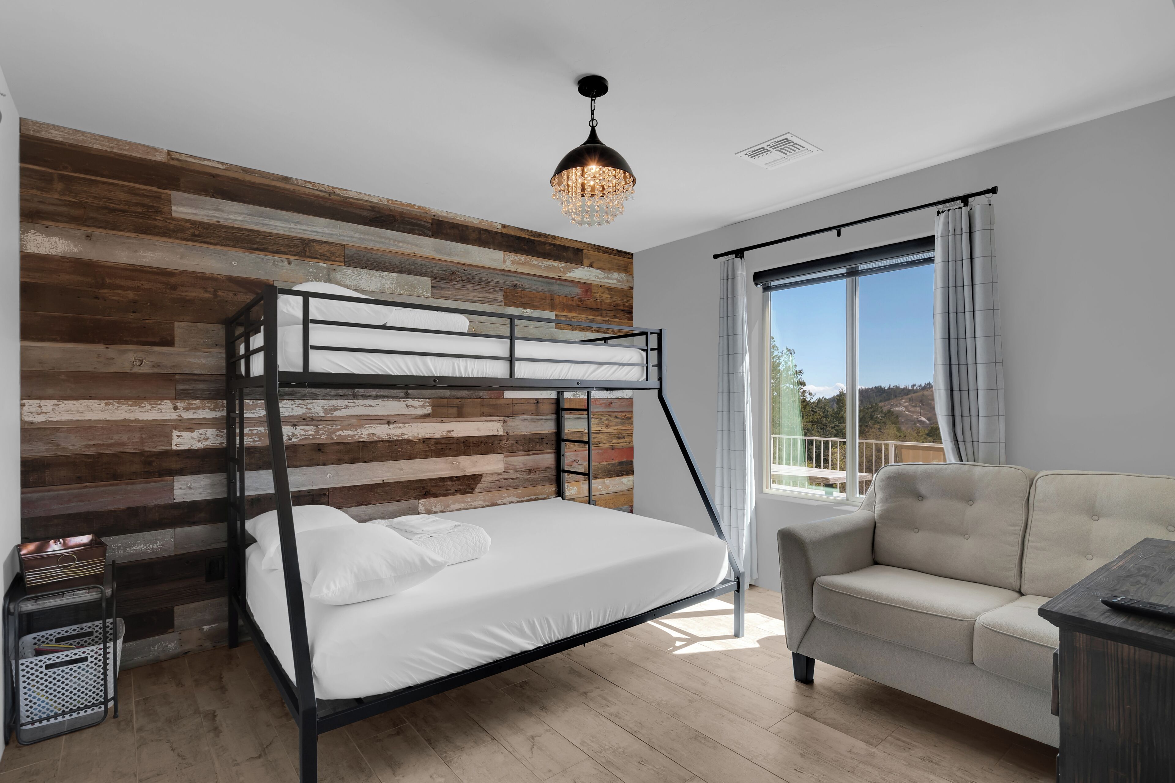 A bunk bed with a wooden wall backdrop, a sofa, and a balcony with a view.
