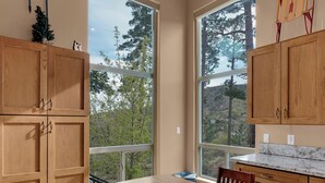 A modern kitchen with wooden cabinets, a large window, and a dining table with chairs. - Ski Tucson Cabin at Mt Lemmon Hotel Overlooking Summerhaven, Arizona (Mount Lemmon)