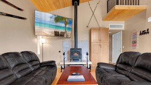 A living room with a fireplace, black leather sofas, a wooden coffee table, and a beach-themed painting on the wall. - Ski Tucson Cabin at Mt Lemmon Hotel Overlooking Summerhaven, Arizona (Mount Lemmon)
