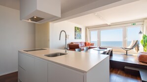 A modern kitchen with a central island, a dining area with a view of the sea, and a seating area with a sofa and chairs. - Studio in Ostend Near Beach and Promenade (Ostend)
