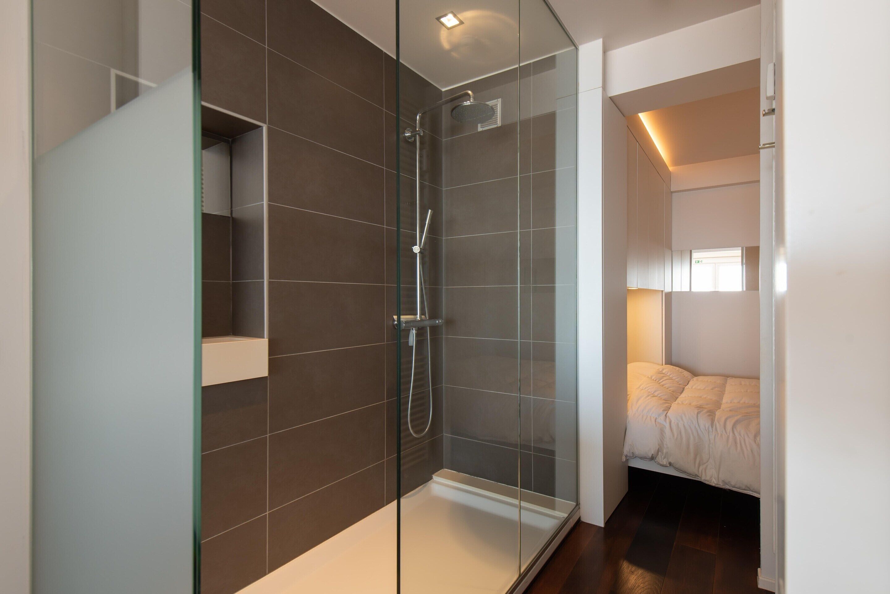 A modern bathroom with a glass shower enclosure, a white sink, and a built-in shelf.