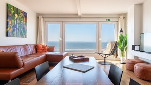 A modern living room with a leather sofa, a dining table, and a view of the sea through large windows. - Studio in Ostend Near Beach and Promenade (Ostend)