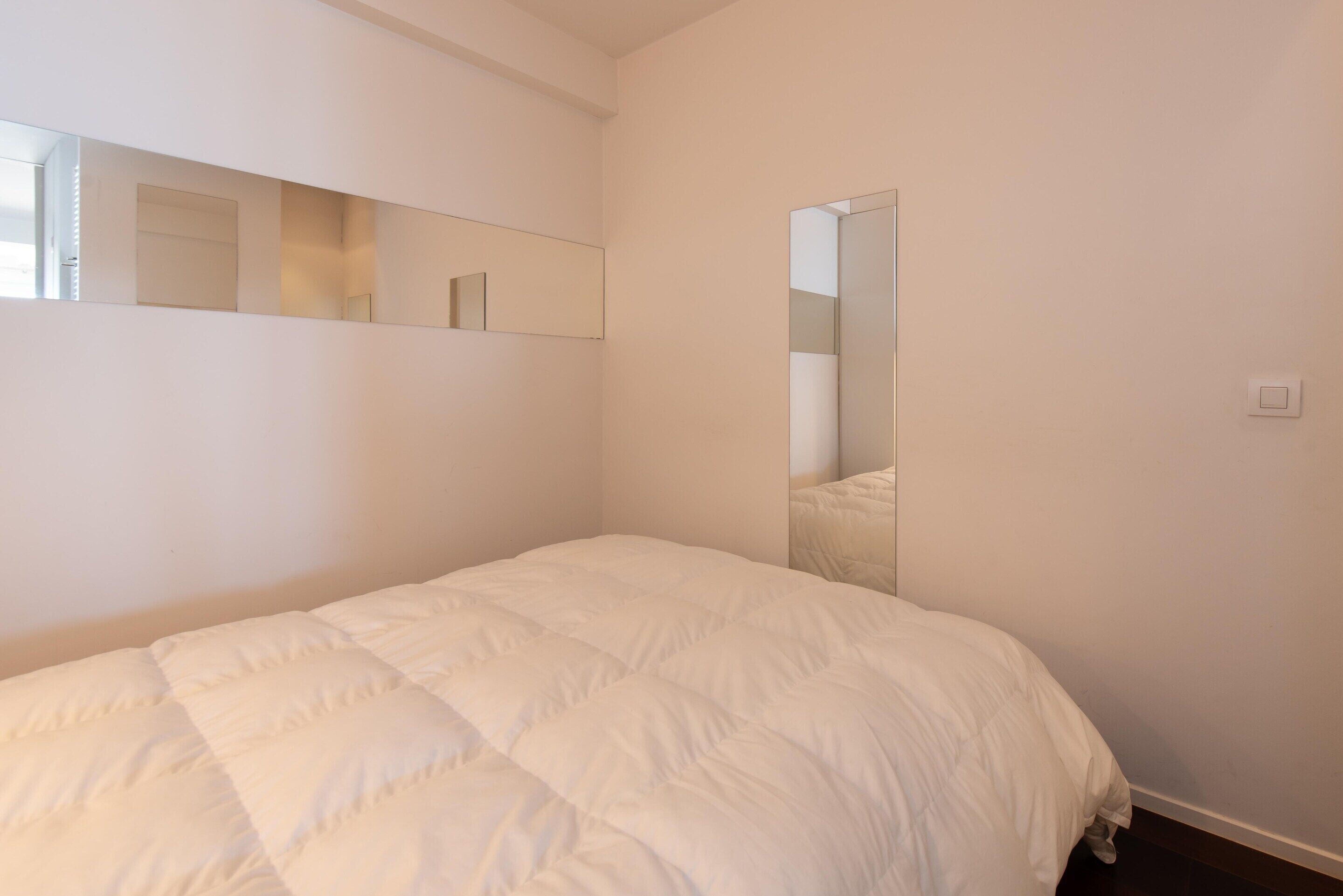 A bedroom with a large bed, a wall-mounted mirror, and a light switch.