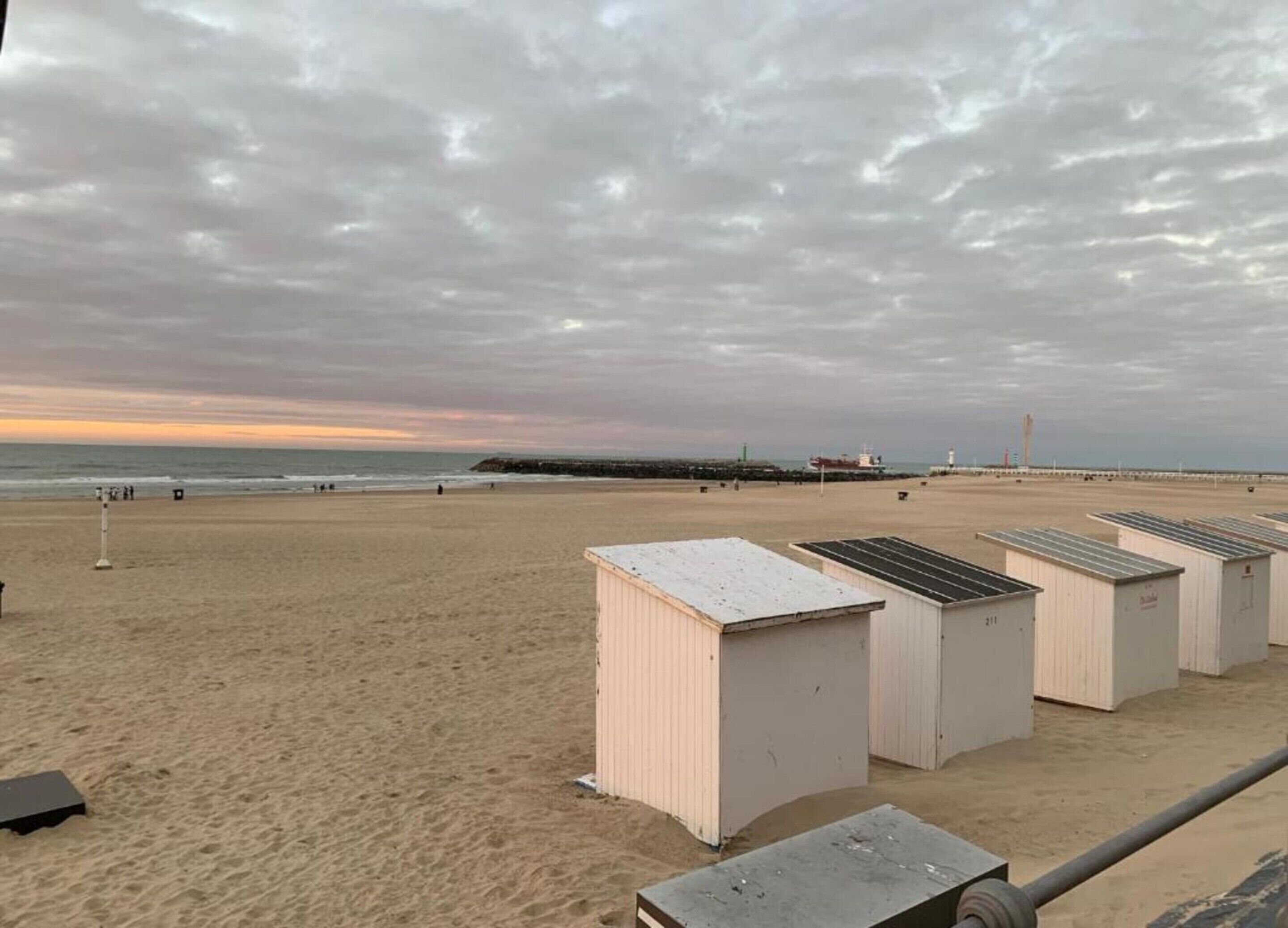 A beach with a row of white beach huts and a pier in the background.