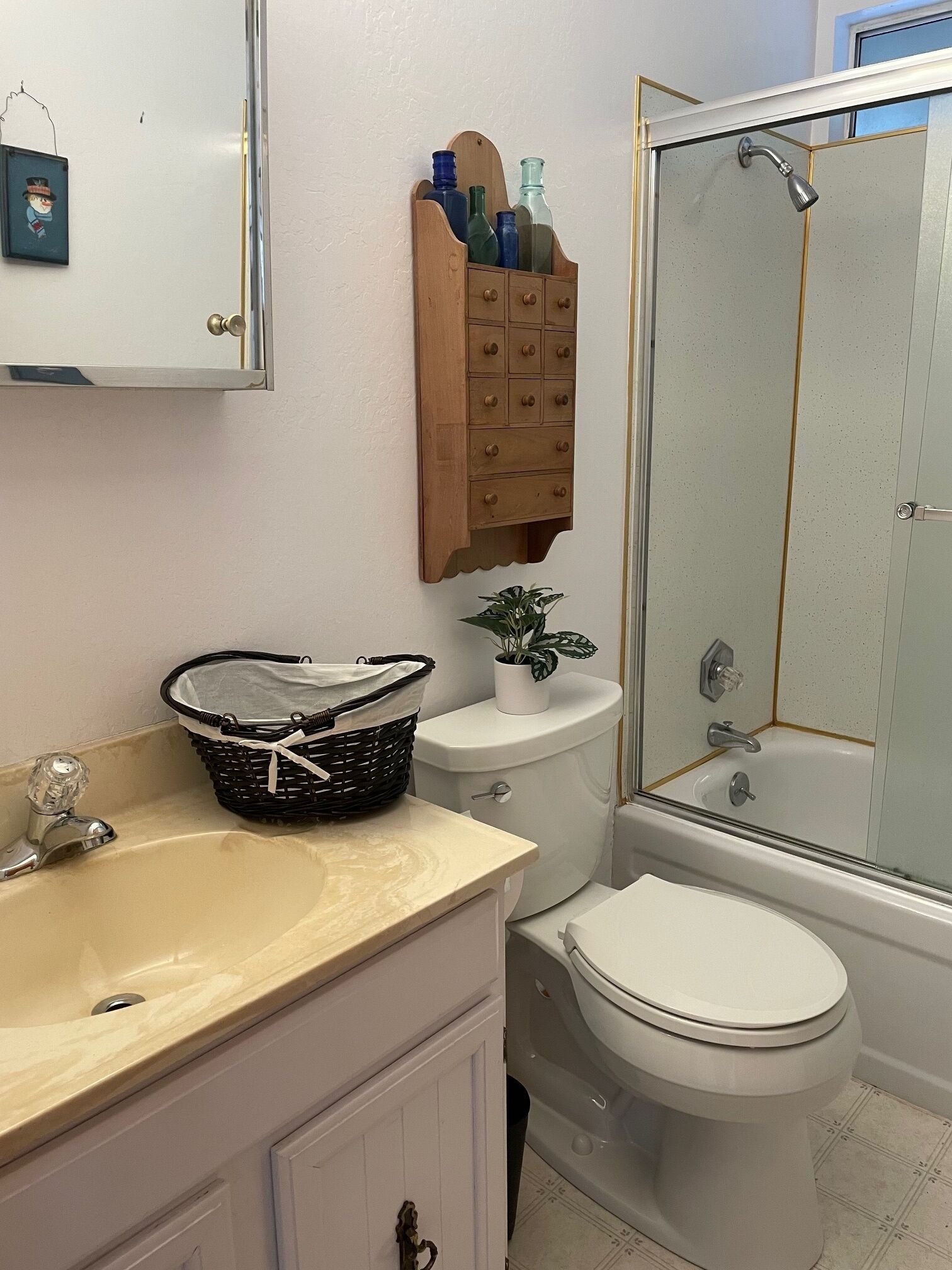 Ein Badezimmer mit Waschbecken, Toilette und Dusche. Über dem Waschbecken befindet sich ein Holz-Arztkorb und auf der Toilette ein kleiner Topfpflanze.