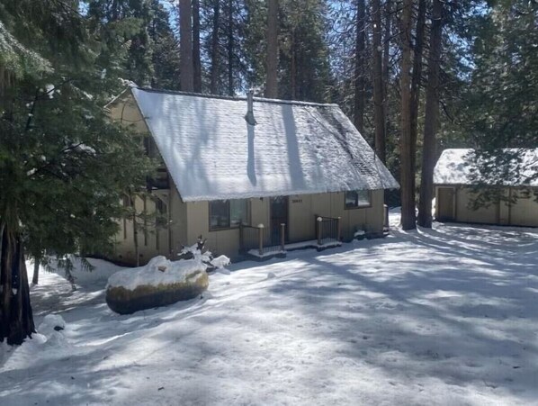 Une cabane au toit en pente, entourée d’un paysage enneigé et d’arbres.