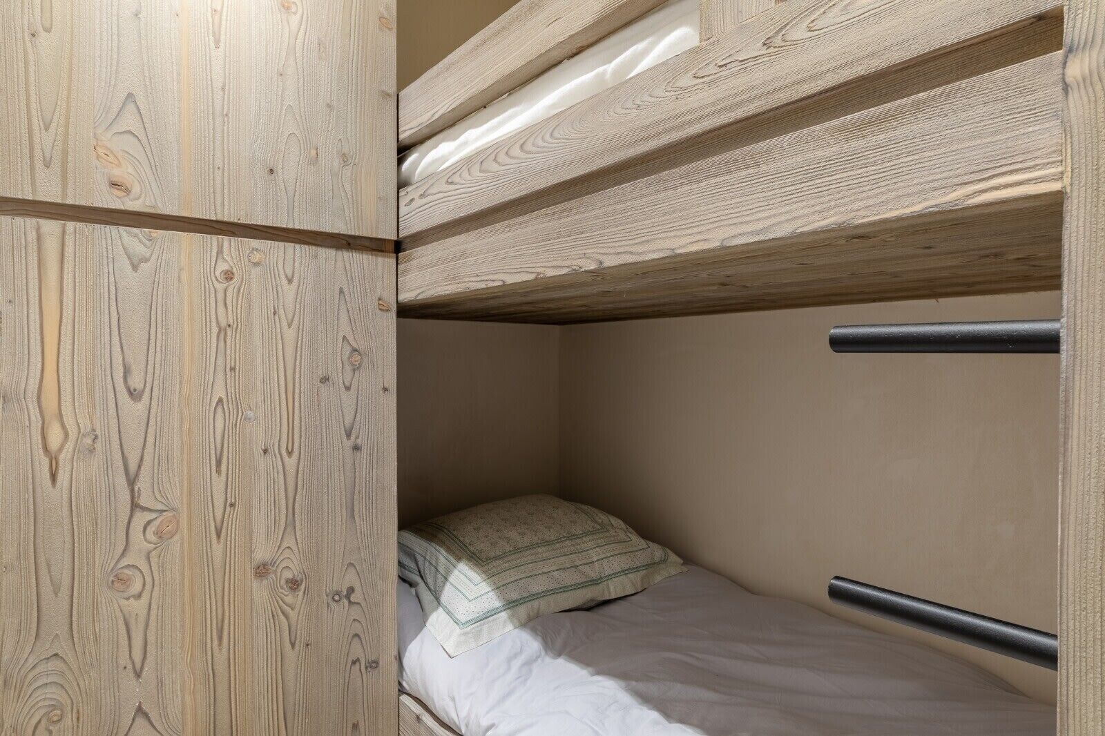 Un lit superposé avec des panneaux en bois et un lit simple avec un oreiller.