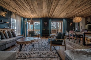 A cozy living room with a wooden ceiling, a sofa, a round coffee table, and a dining area with chairs and a table.