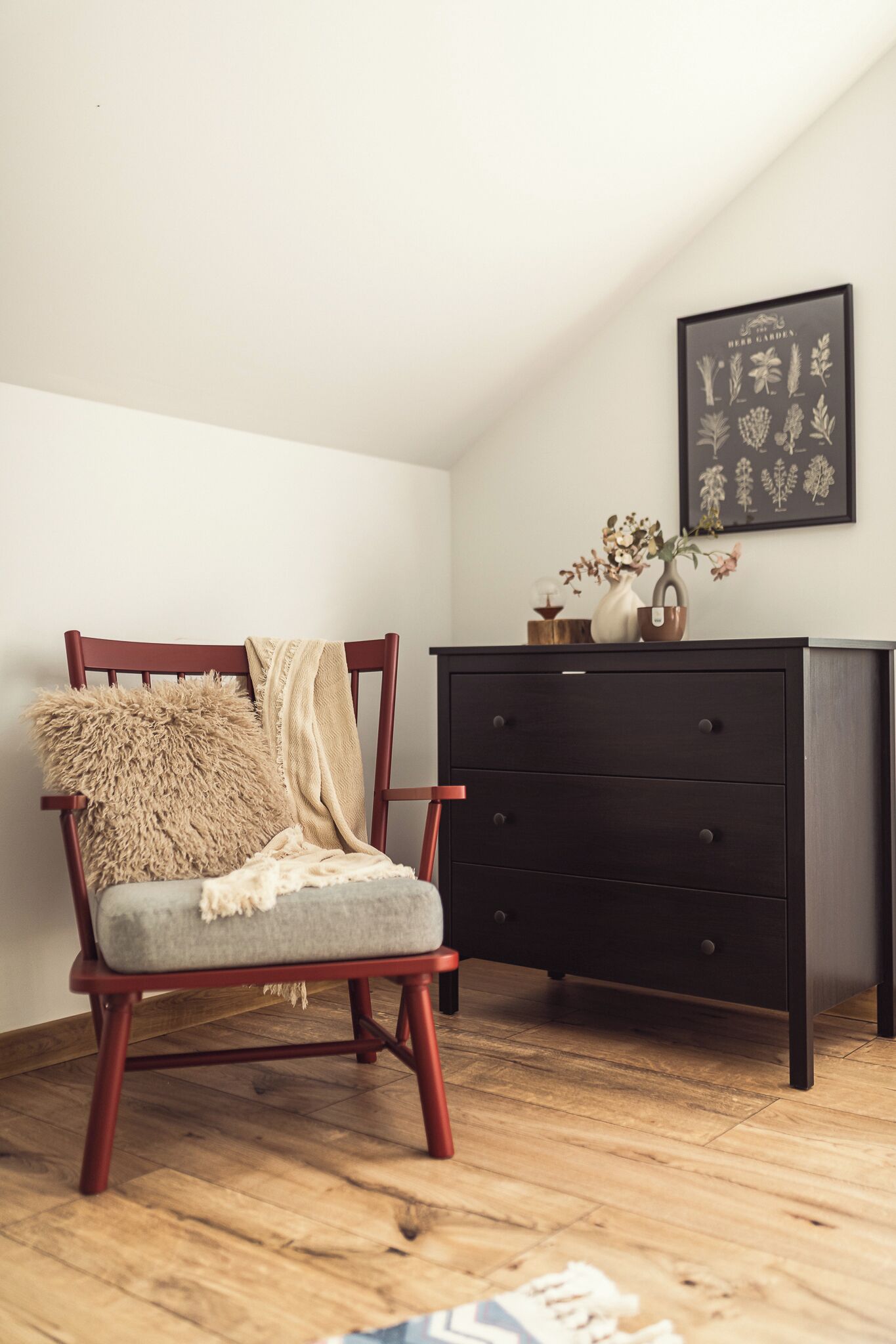 Une pièce comprenant une chaise en bois, une commode sombre et une estampe botanique encadrée accrochée au mur.