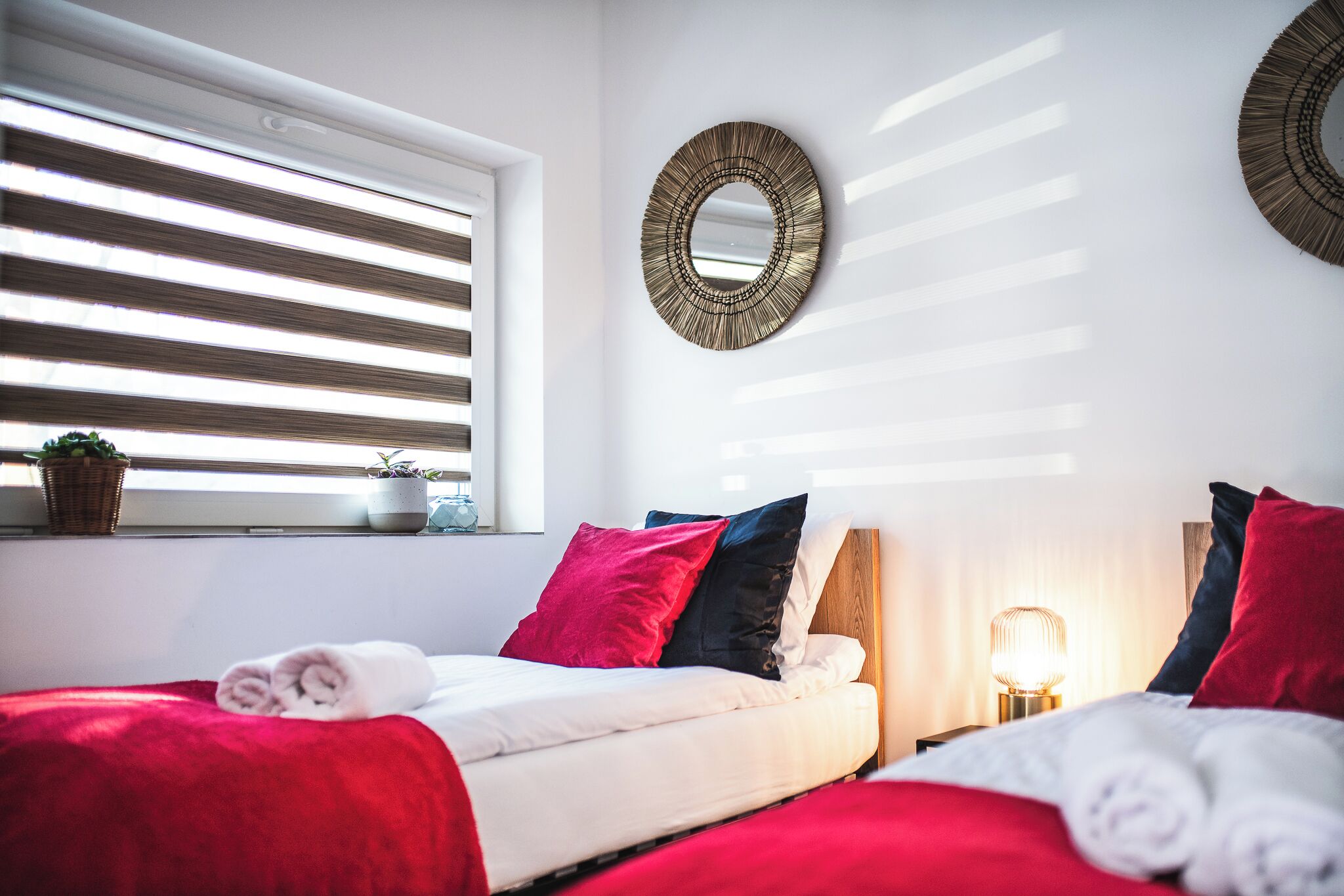 A neatly made bed with red and white bedding, a bedside lamp, and a wall-mounted mirror.