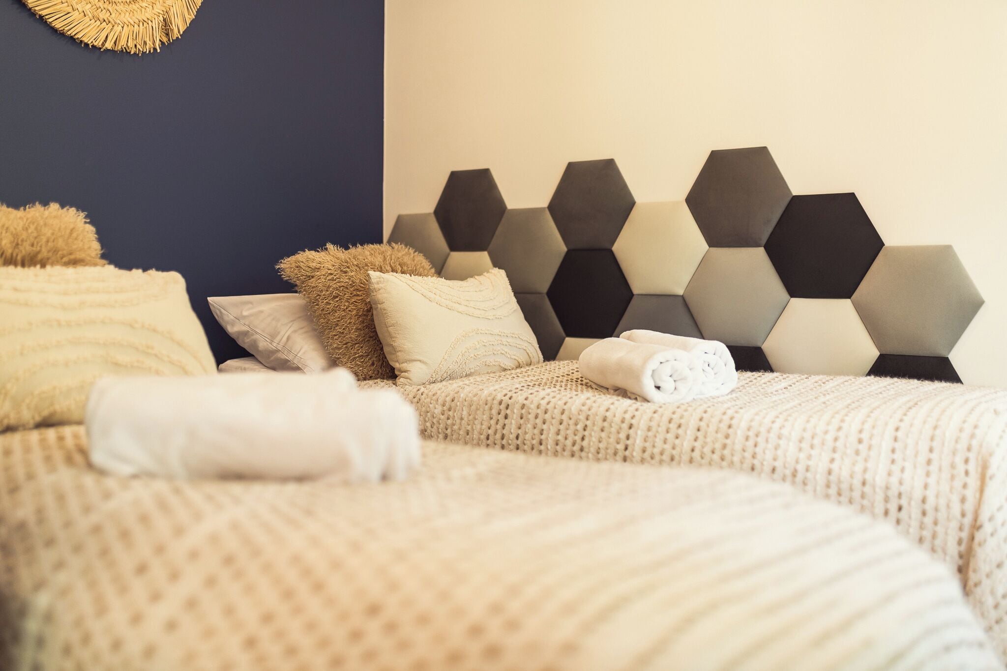 A neatly made bed with a geometric headboard, a woven wall decoration, and a textured blanket.