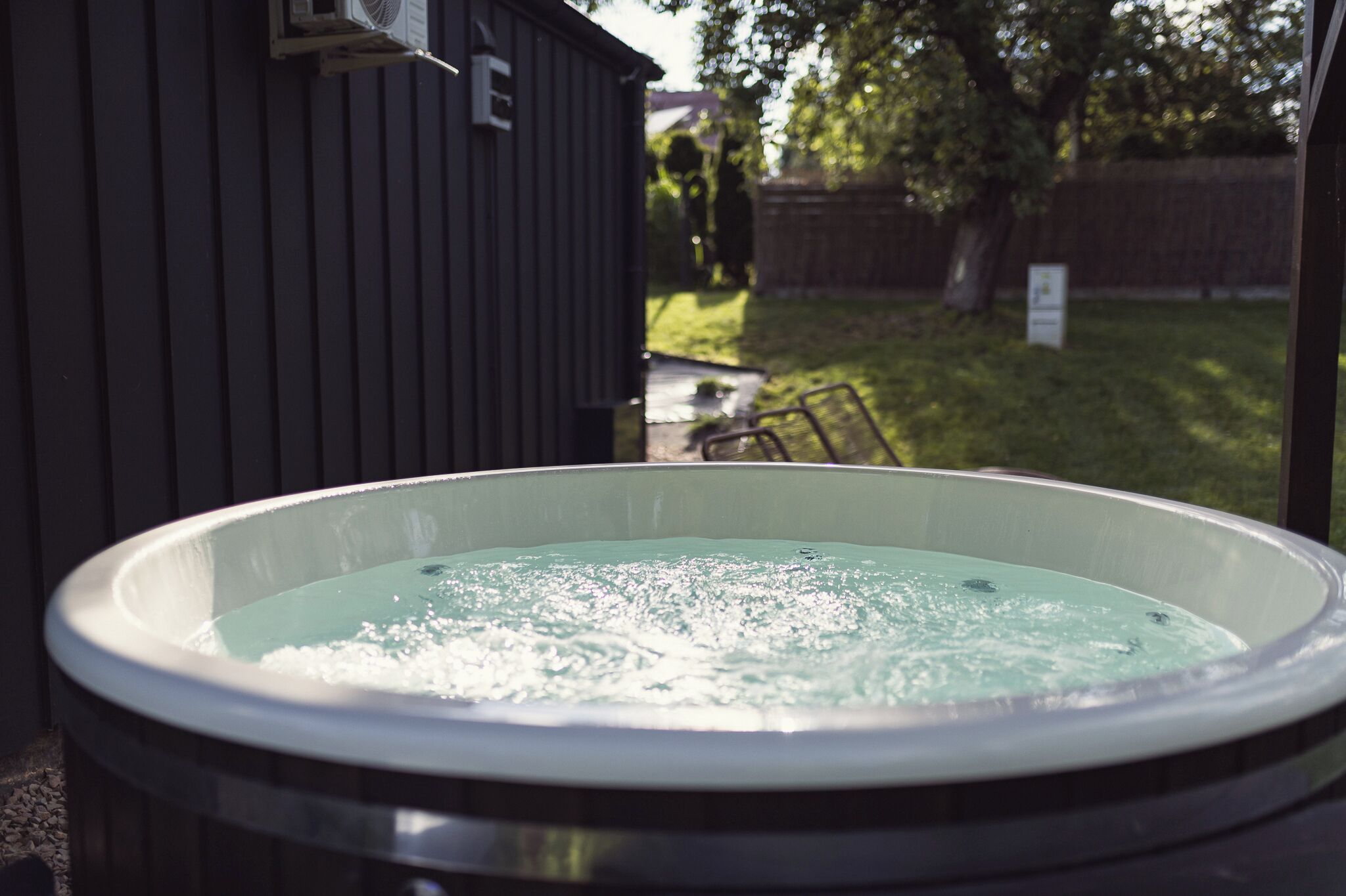 A hot tub with a view of a backyard, a wooden shed, and a lawn.